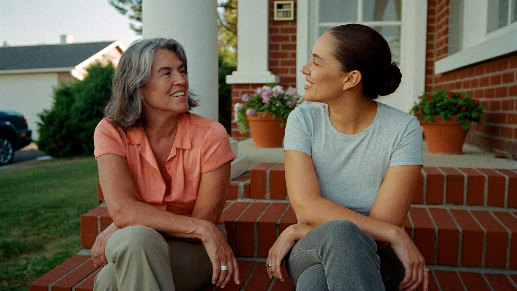 A woman in her late fifties talks with her adult daughter on the front porch steps of a brick home, illustrating how an annuity passes to a named beneficiary